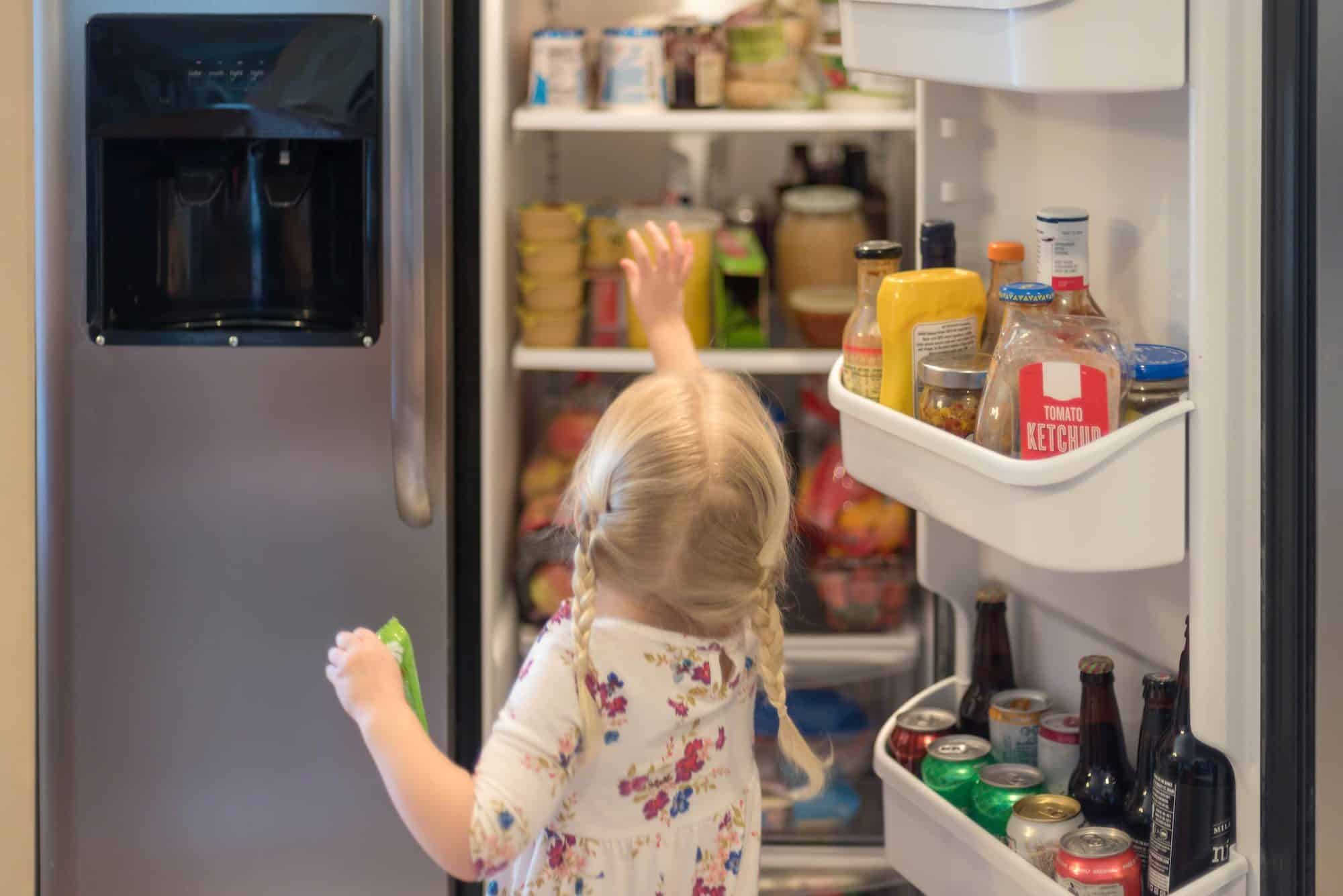 Child reaching in open refrigerator