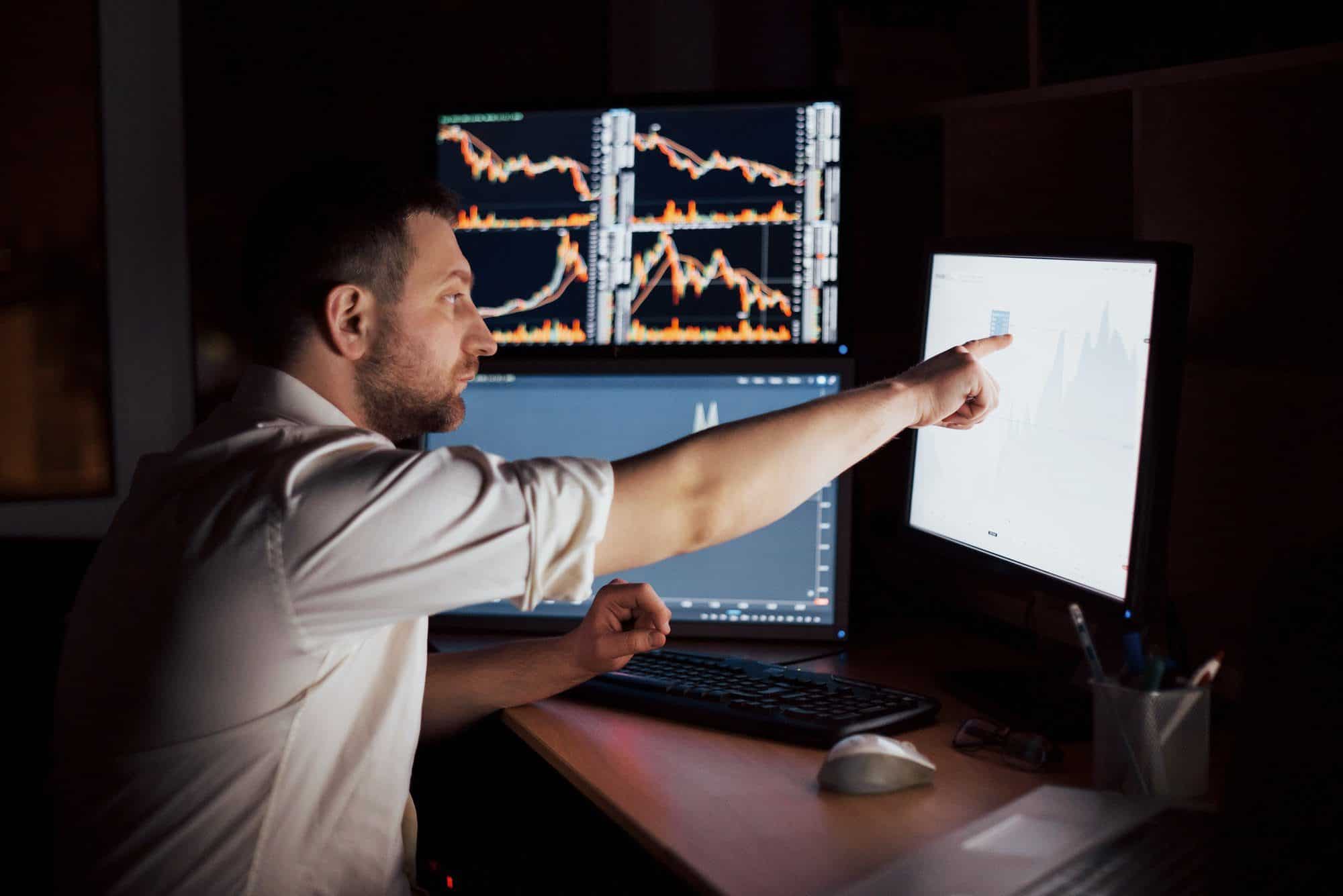 Stockbroker in shirt is working in a monitoring room with display screens. Stock Exchange Trading