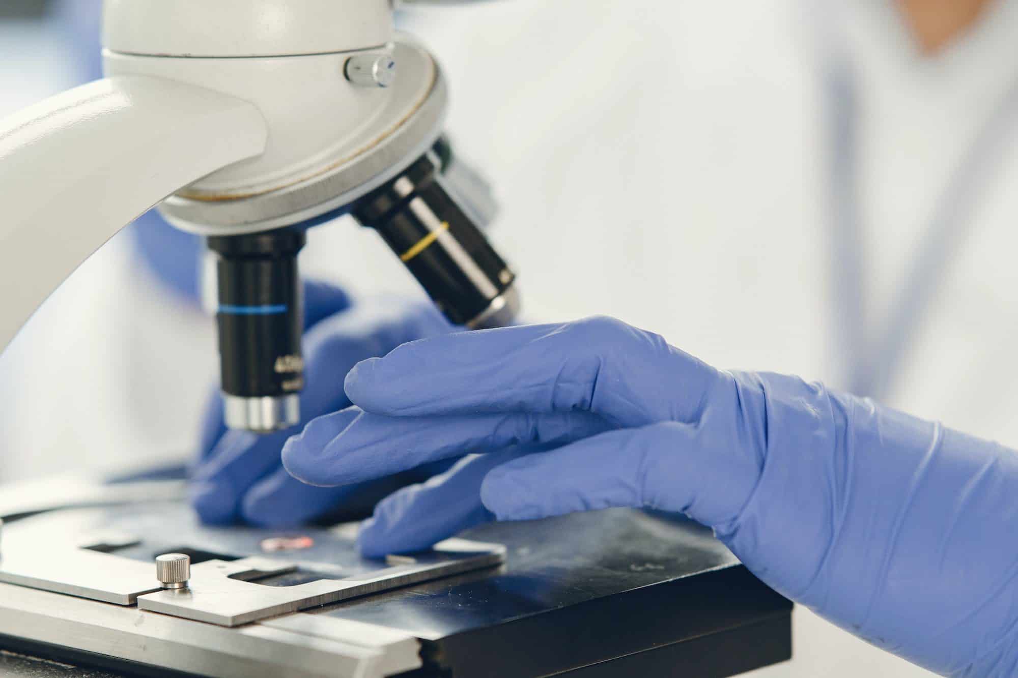 Unrecognizable lab worker inspecting blood sample under microscope